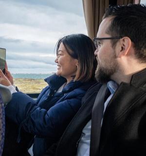 a man and woman sitting on a train looking at a cell phone