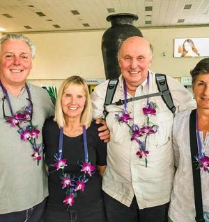 tři lidé pózují pro fotografii s květinami na krku