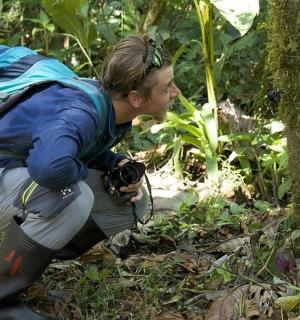 a man with a camera kneeling in the forest