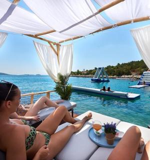 स्नान सूट पहने दो लड़कियाँ पानी के सामने सोफे पर बैठी हैं