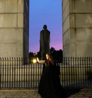 žena držící svíčku před sochou