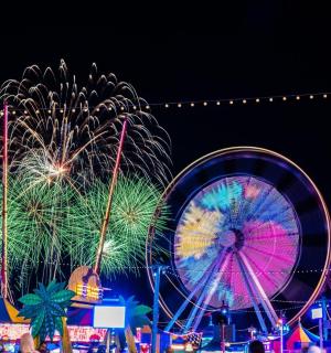 a carnival with fireworks and a ferris wheel at night