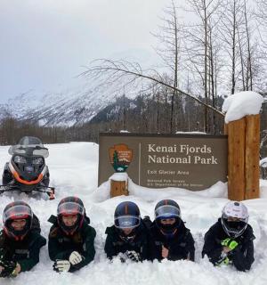 一群人坐在雪地里，前面是一块标志牌