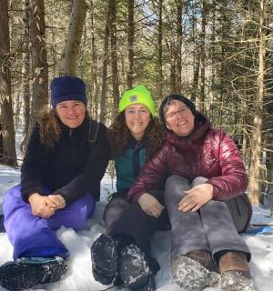 three people sitting in the snow in the woods