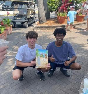 two young men holding up a gift in a park