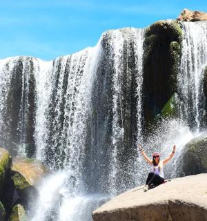 一位女士站在瀑布前的岩石上