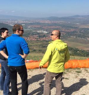 tři muži stojící na vrcholu kopce s velkým padákem