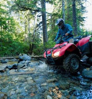 eine Person auf einem Geländefahrzeug, die einen Bach überquert