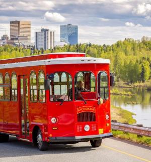 a red bus driving down a road next to a lake
