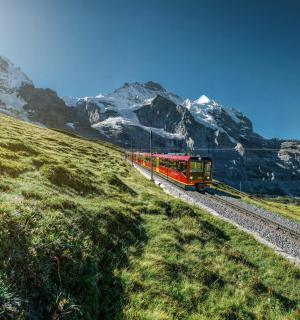 červený vlak jedoucí po kolejích v horách