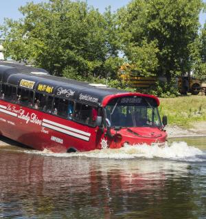 一辆红色巴士在水中行驶在一条河里