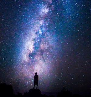 muž stojící na skále a dívající se na vesmír