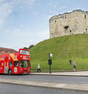a red double decker bus driving past a castle