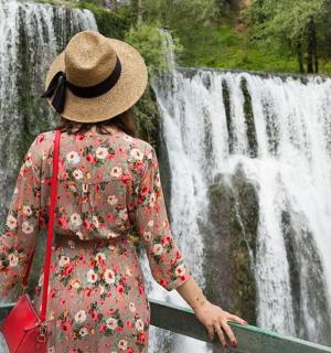 a woman in a hat standing in front of a waterfall