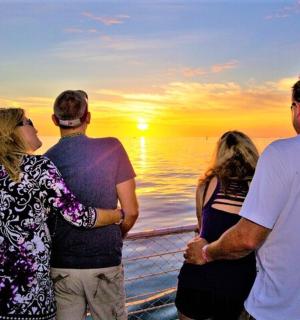 a group of people standing on a cruise ship looking at the sunset