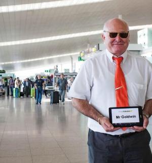 vyras, dėvintis raudoną kaklaraištį ir laikantis ženklą oro uoste