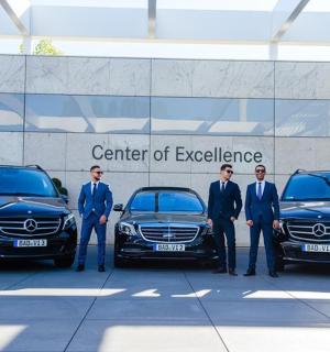 a group of men in suits standing in front of two cars