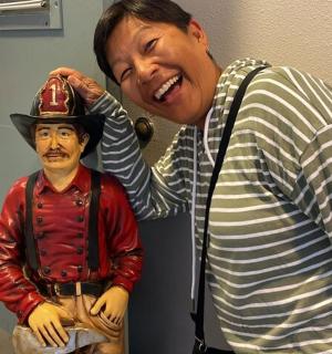 一名男子站在一尊戴帽子男子雕像旁边