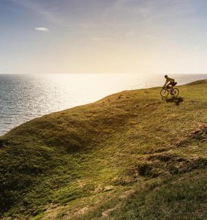 a person riding a bike on a hill near the ocean