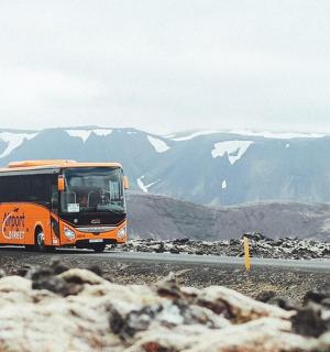 an orange bus driving down a road with mountains in the background