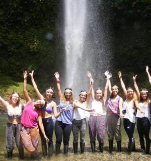 a group of women standing in the water in front of a waterfall