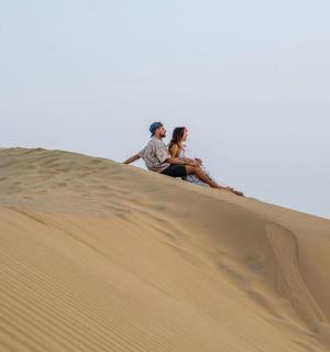 dva lidé sedící na vrcholu písečné duny