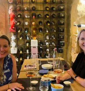 two women sitting at a table with wine bottles