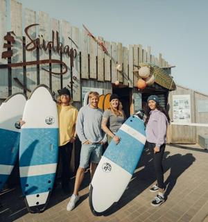 eine Gruppe von Menschen steht mit Surfbrettern vor einem Gebäude