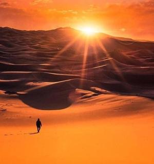 a man walking in the desert at sunset