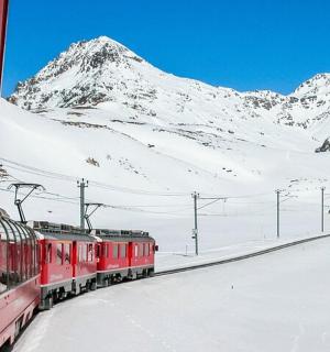 červený vlak jedoucí kolem zasněžené hory