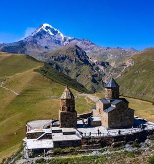an old church on a hill with mountains in the background