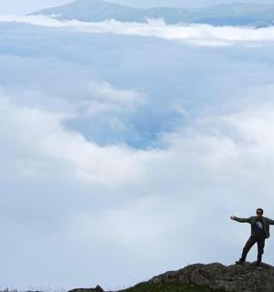 muž stojící na vrcholu hory s rozpaženýma rukama
