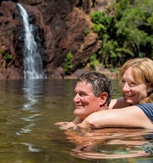a man and woman swimming in a lake with a waterfall