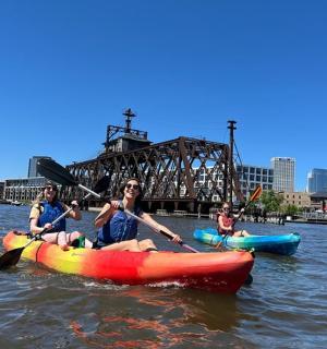 三个人在桥前的河上划皮划艇