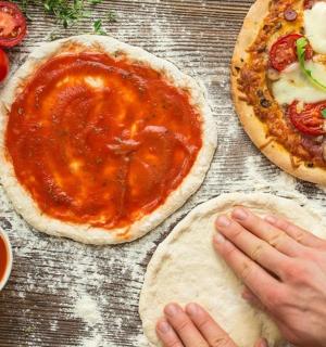 两个披萨放在木桌上，旁边还有人在做披萨