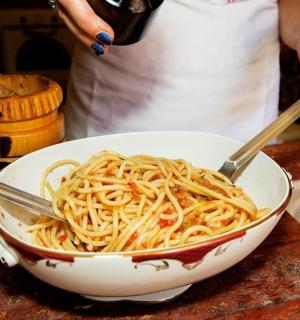 a person is preparing pasta in a bowl with tongs