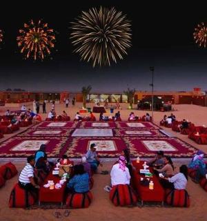 skupina lidí sedících u stolů s ohňostrojem v pozadí