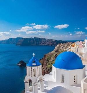 eine Gruppe weißer Gebäude mit blauen Kuppeln und dem Meer