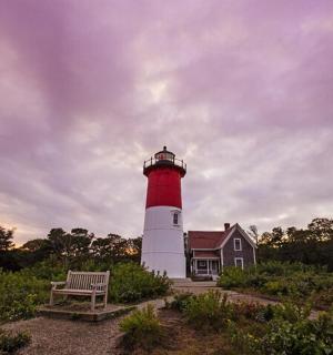 一座红白相间的灯塔，房子前有一张长椅