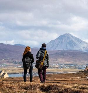 a couple standing on a hill looking at a mountain