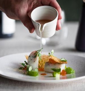 osoba nalévající omáčku na talíř s jídlem