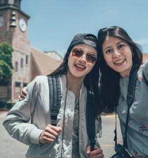 two women standing next to each other in front of a clock tower