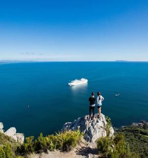 dva lidé stojící na vrcholu útesu s lodí ve vodě