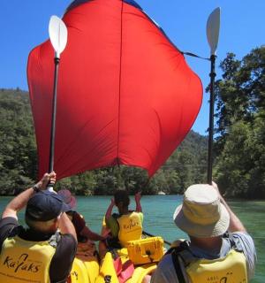 skupina lidí v lodi s červenou plachtou