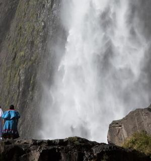 two people standing on rocks looking at a waterfall