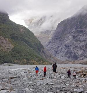 a group of people walking on a rocky river in a mountain