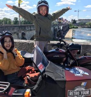 一名女子站在摩托车旁，双臂高举