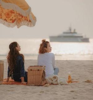 two women sitting on the beach under an umbrella
