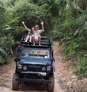 two people sitting on top of a jeep on a dirt road