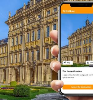 eine Person, die vor einem Gebäude ein Mobiltelefon hochhält